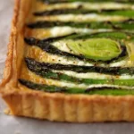 Asparagus Gruyere Tart garnished with herbs on a wooden board