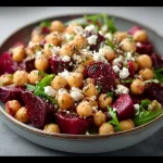 Chickpea, beet, and feta salad in a bowl with fresh greens and colorful vegetables.