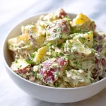 Creamy red potato salad in a bowl, garnished with herbs.