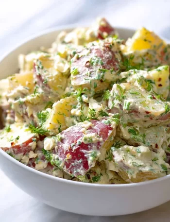 Creamy red potato salad in a bowl, garnished with herbs.