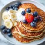Three-ingredient high protein pancakes stacked on a plate with fresh fruit