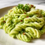 A bowl of creamy avocado broccoli pasta garnished with fresh herbs.