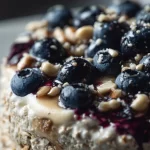 Delicious blueberry cheesecake overnight oats in a glass topped with fresh blueberries.