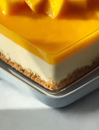 A slice of creamy mango cheesecake topped with fresh mango slices.