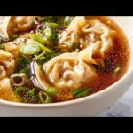 Bowl of homemade wonton soup with fresh ingredients and wontons.