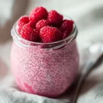 Bowl of raspberry chia pudding sweetened with maple syrup, topped with fresh berries