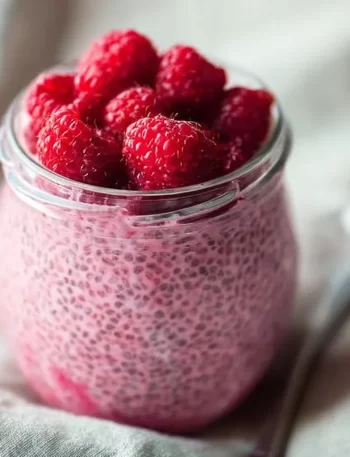Bowl of raspberry chia pudding sweetened with maple syrup, topped with fresh berries