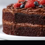 A slice of ultimate gluten free chocolate cake topped with rich chocolate frosting.
