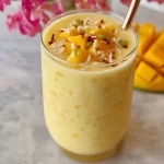 Creamy mango smoothie drink with fresh mango slices on top