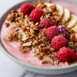 Delicious pink raspberry smoothie bowl topped with fresh berries and granola.