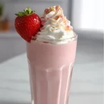 Delicious strawberry protein shake in a glass with fresh strawberries on top