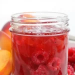Three jars of homemade raspberry peach jam on a wooden table