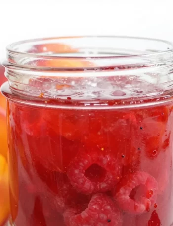 Three jars of homemade raspberry peach jam on a wooden table