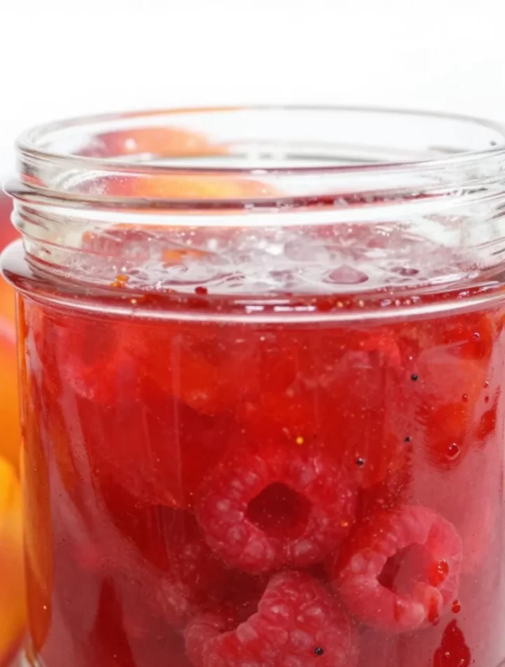 Three jars of homemade raspberry peach jam on a wooden table