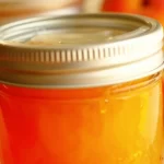 Homemade easy peach jam in a jar with fresh peaches and bread.