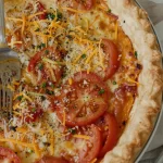 Slice of Kentucky Tomato Pie served with fresh herbs and a crispy crust