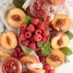 A jar of Minute Raspberry Peach Jam on a breakfast table with toast and fresh peaches.