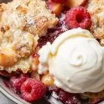 Delicious Raspberry Ripple Peach Cobbler topped with fresh raspberries and golden crust.